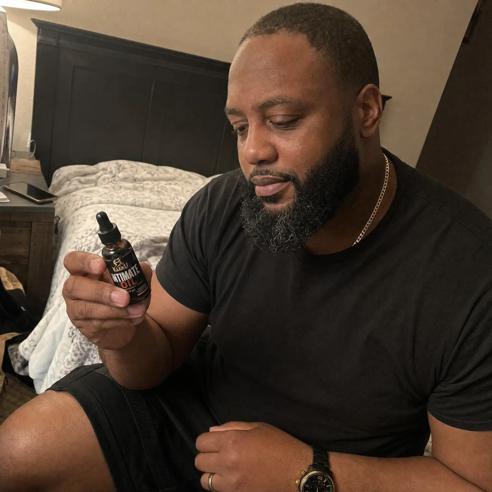 Man holding a Kleku Intimate Oil bottle beside his bed at night