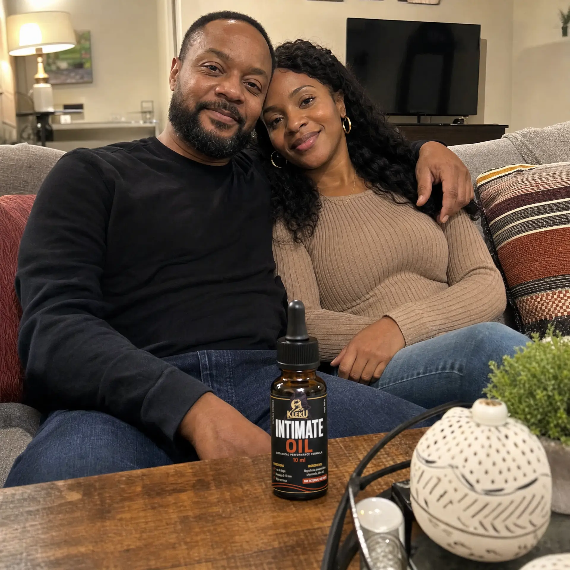 A couple sitting close together on a couch with a Kleku Intimate Oil bottle on the table